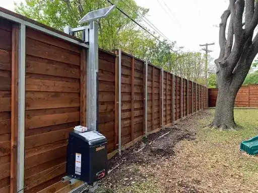 Solar-powered sliding gate operator on a horizontal cedar fence